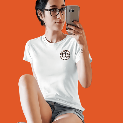 Woman wearing a white "It's Just Yoga" tee, posing with a phone against an orange background.