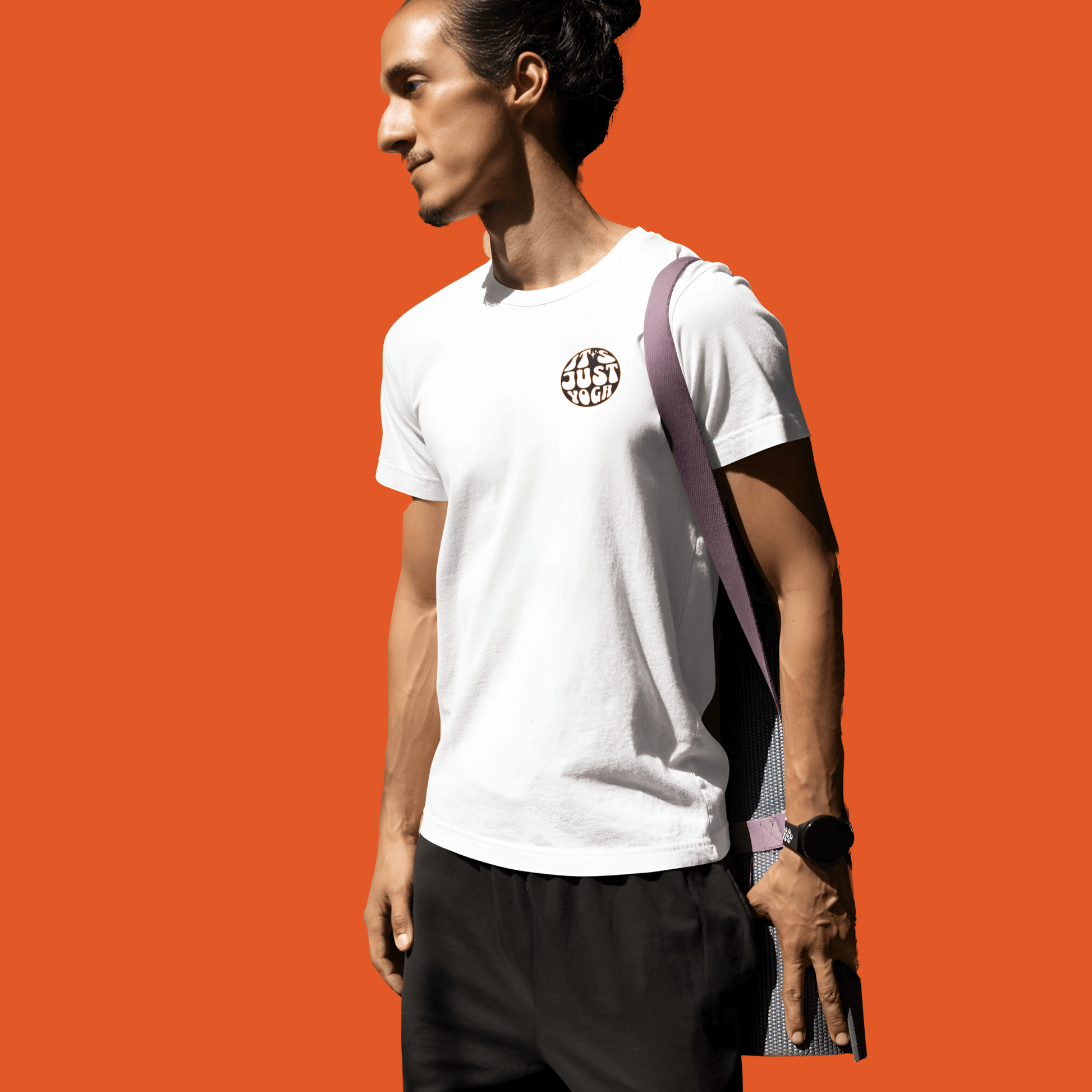 Unisex white tee with "It's Just Yoga" design, worn by a man against an orange background, perfect for yoga enthusiasts.